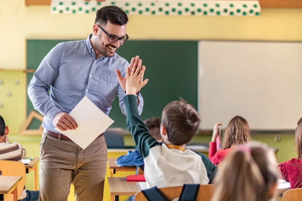 Lehrer mit Hemd und Brille gibt einem sitzenden Schüler im Klassenzimmer einen High-Five
